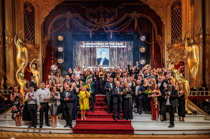 crowd posing on stage in front of a screen with donald sidebottom on, the winner of the lancastrian of the year award
