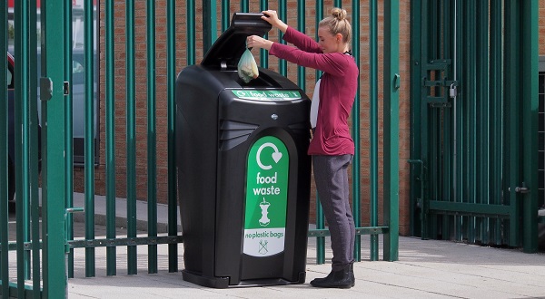 A woman disposing of food waste outside of a multi-occupancy building