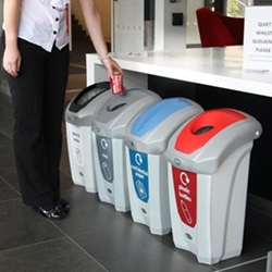 someone disposing of a can in a recycling station with four nexus 30 recycling bins with different apertures