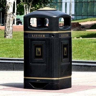A black Glasdon Jubilee 100 litter bin standing in the centre of a plaza with green fields and a tree in the background